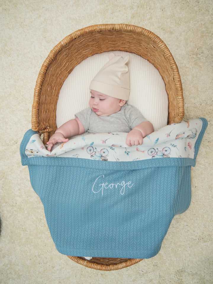 Mouliss baby in basket with personalized blue cable knit baby blanket, bicycle muslin, embroidered name