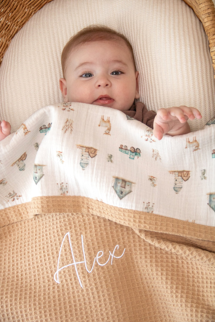 Mouliss personalized caramel waffle baby blanket draped in basket with village animal muslin