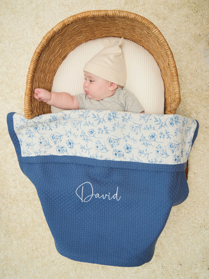 Mouliss baby in basket with personalized navy waffle baby blanket, blue floral muslin, embroidered name