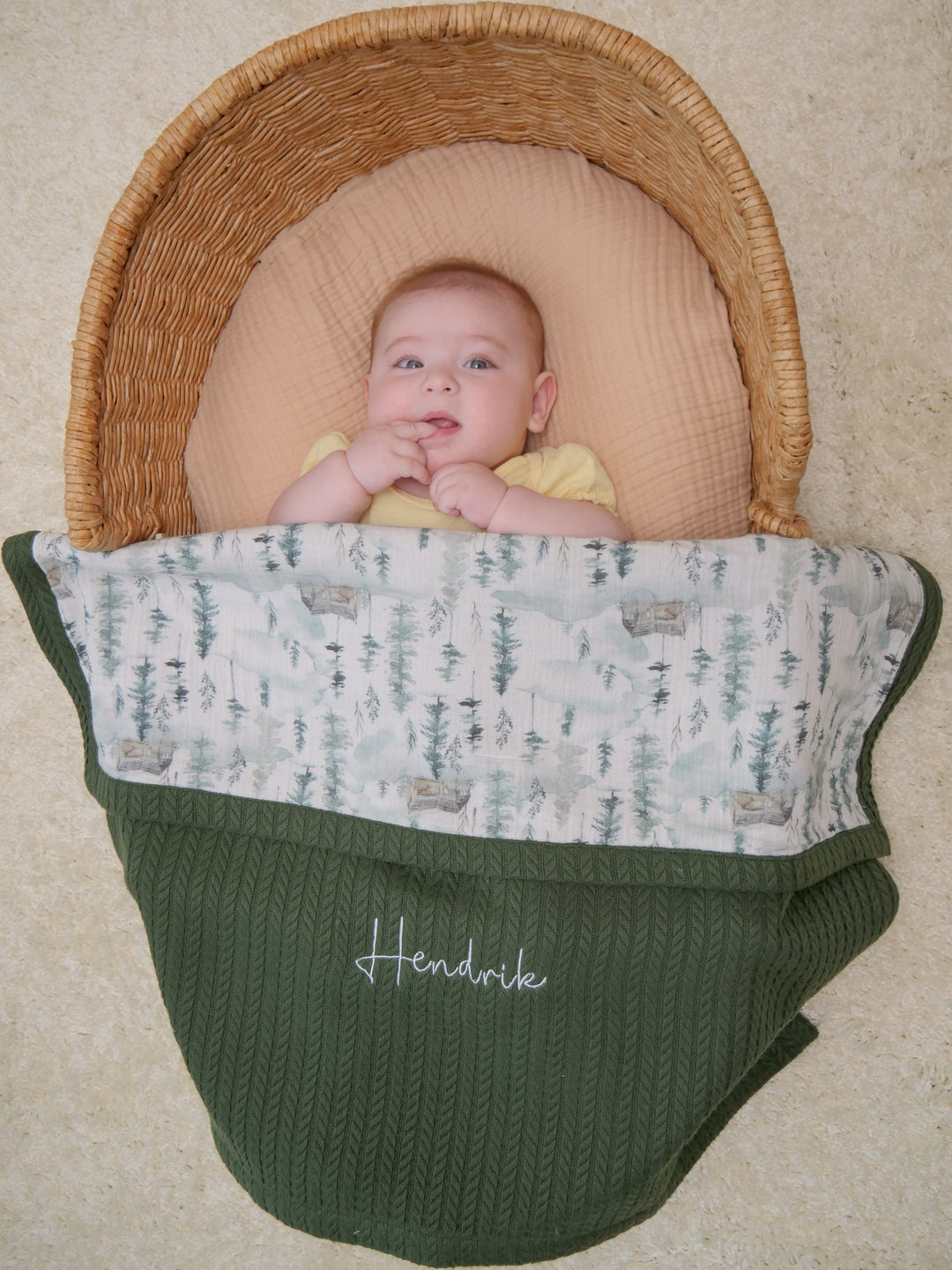 Mouliss baby in basket with personalized green cable knit baby blanket, mountain pine muslin, embroidered name