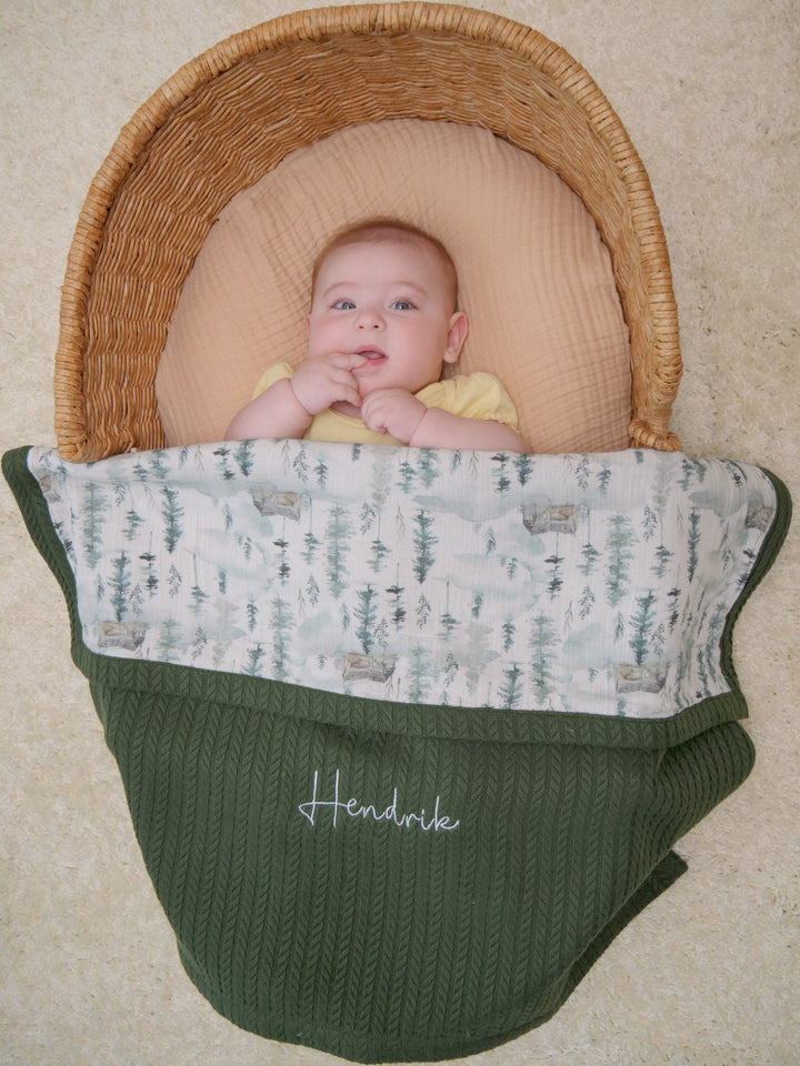 Mouliss baby in basket with personalized green cable knit baby blanket, mountain pine muslin, embroidered name
