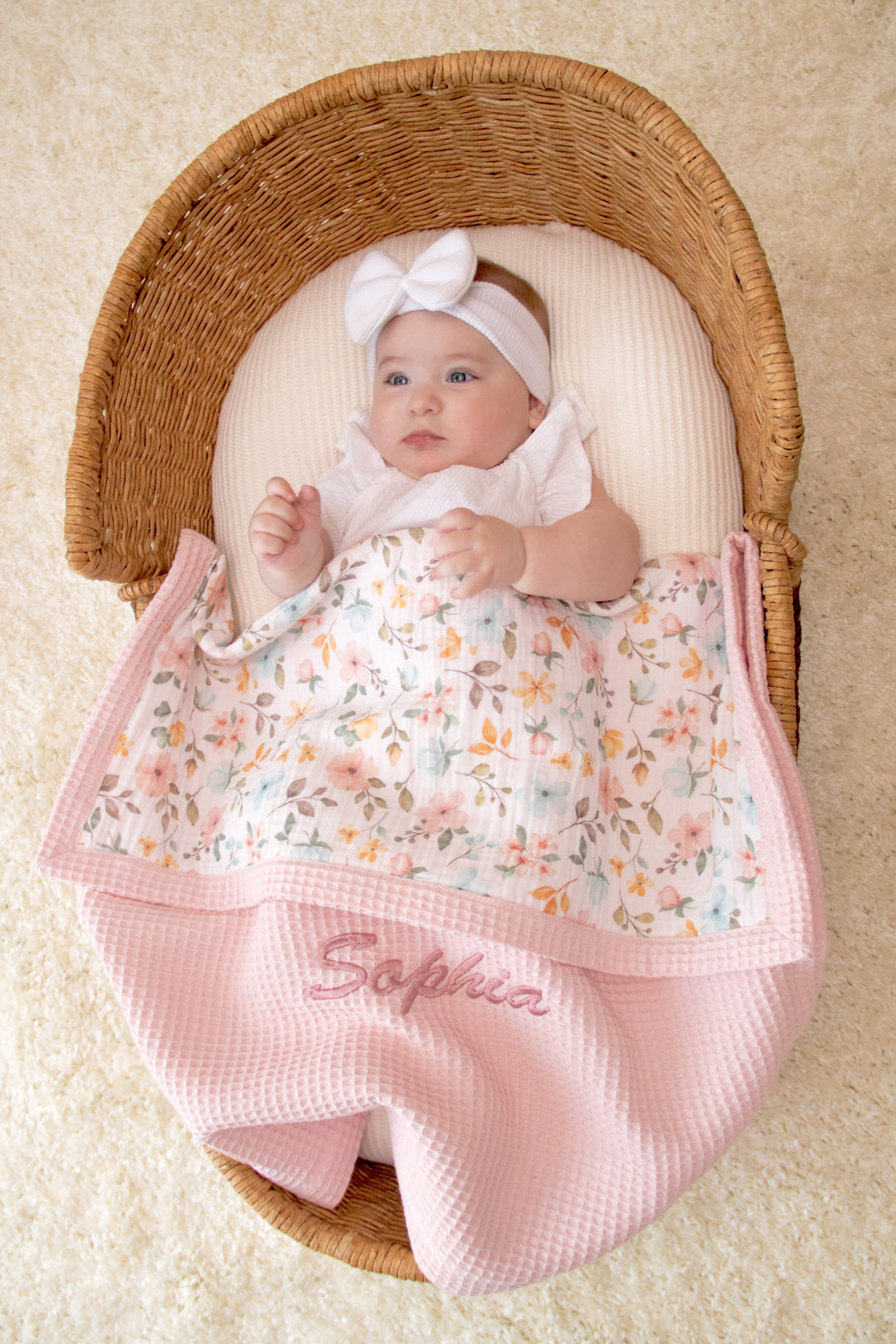 Mouliss personalized pink waffle baby blanket draped in basket with watercolor floral muslin