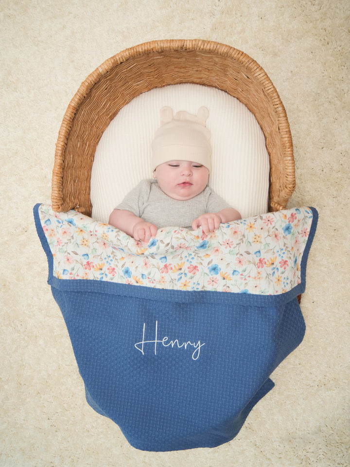 Mouliss personalized navy waffle baby blanket draped in basket with colorful floral muslin
