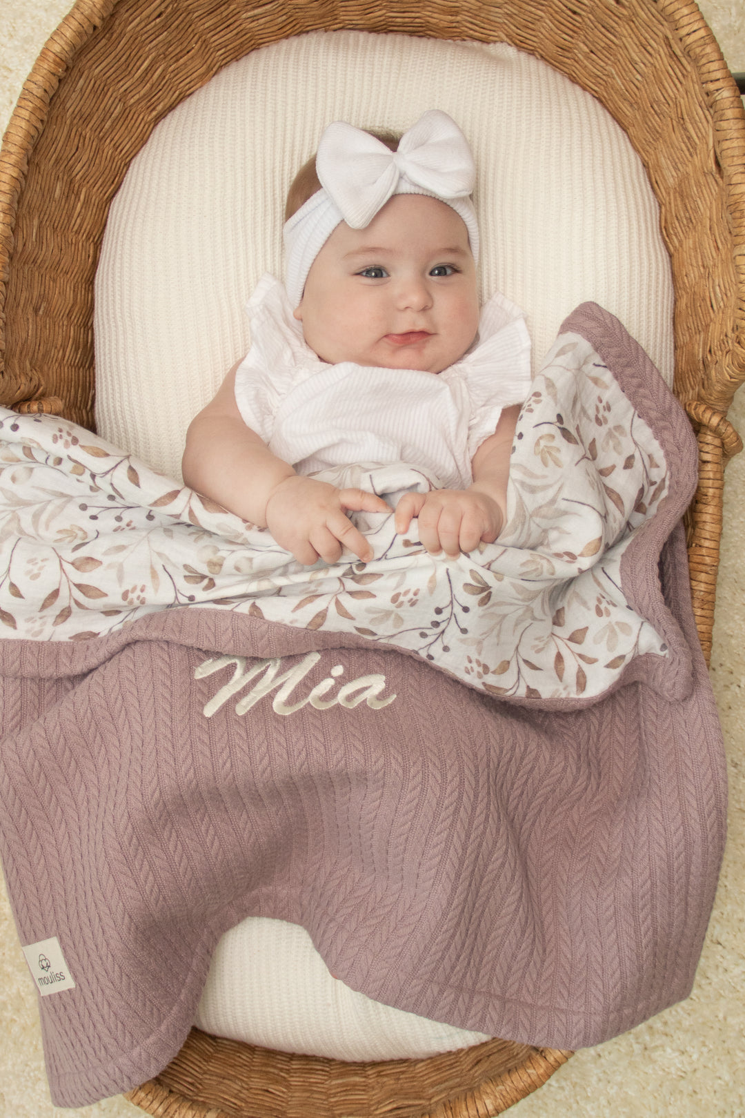 Mouliss personalized mauve baby blanket draped in basket with botanical leaf muslin