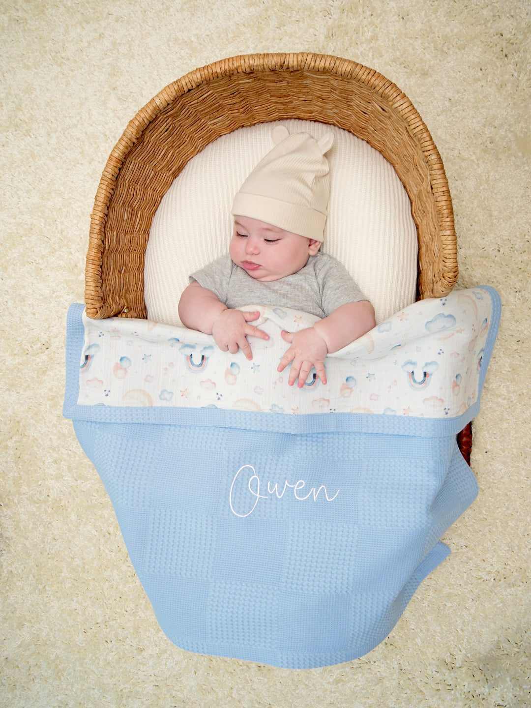 Mouliss baby in basket with personalized blue waffle baby blanket, rainbow muslin, embroidered name