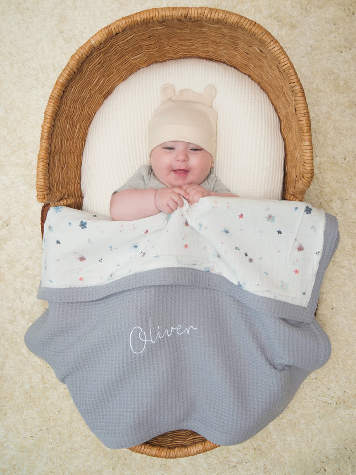 Mouliss baby in basket with personalized grey waffle baby blanket, floral muslin, embroidered name