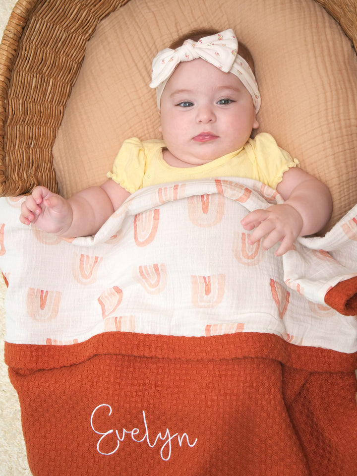 Mouliss close-up of embroidered name on personalized rust waffle baby blanket with rainbow muslin