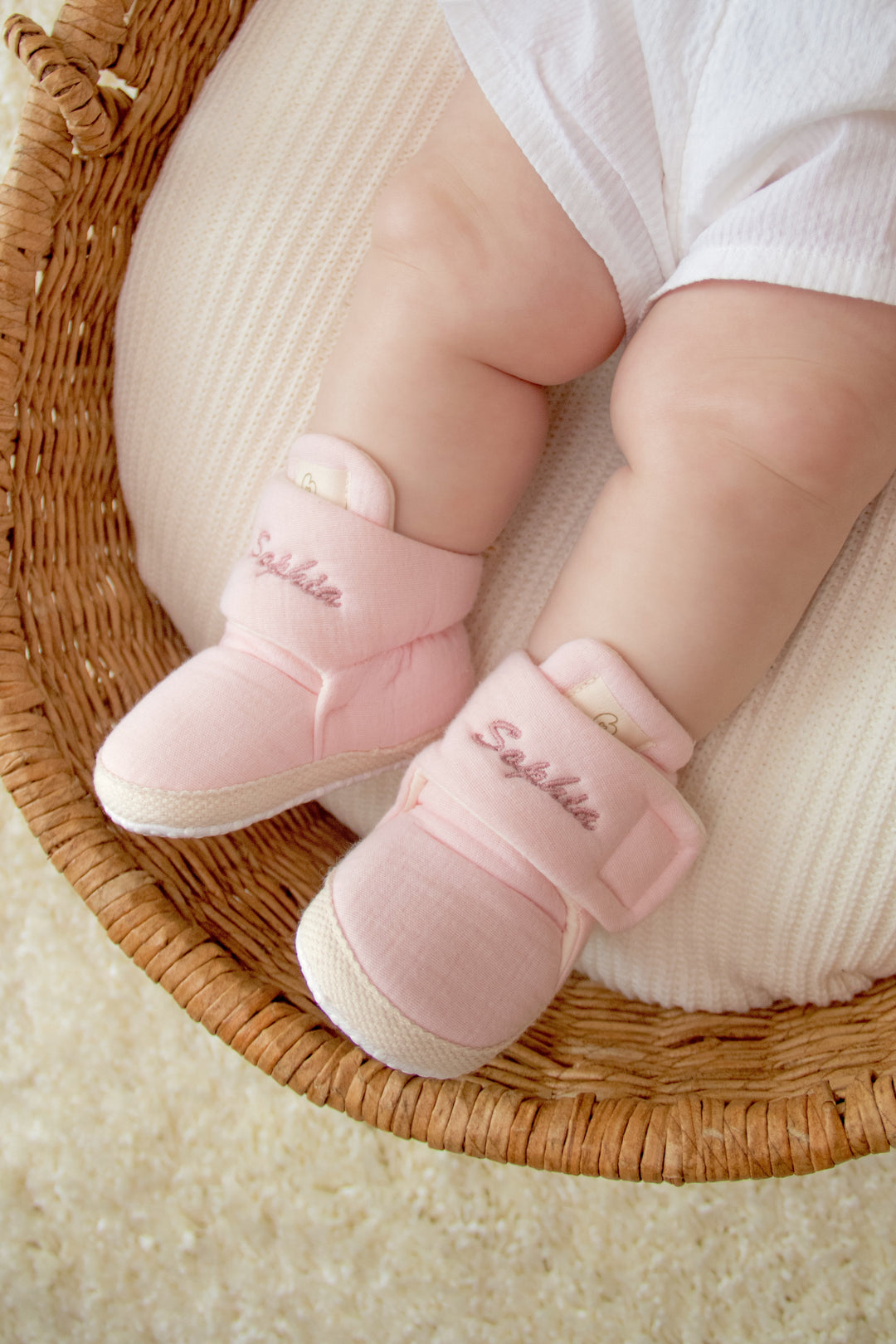 Mouliss baby wearing personalized pink baby booties with embroidered name, in basket