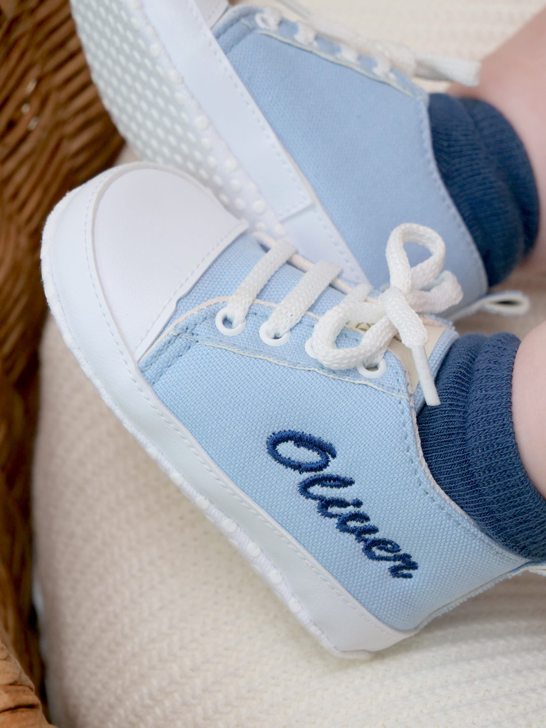 Mouliss baby wearing personalized light blue canvas baby shoes with embroidered name, in basket