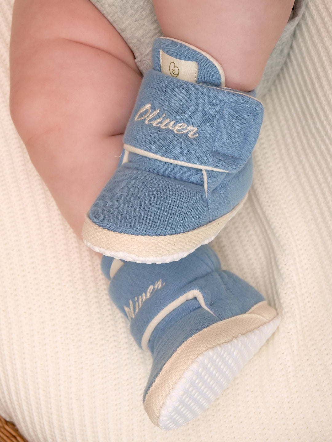 Mouliss baby wearing personalized denim blue baby booties with embroidered name, in basket
