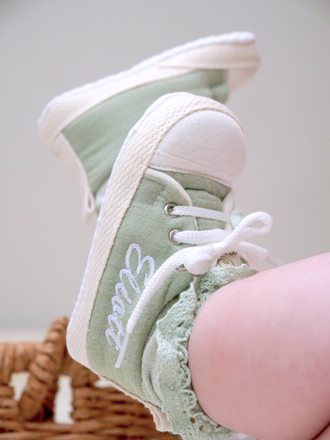 Mouliss personalized sage green baby shoes with embroidered name, on baby in basket