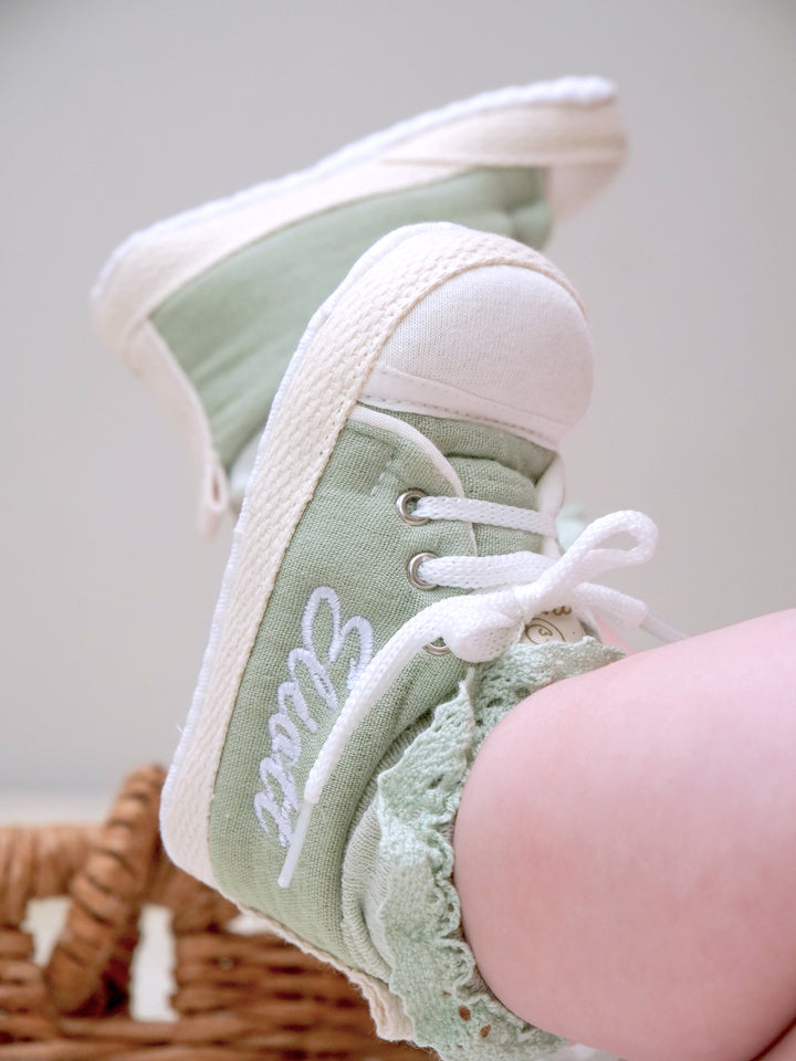 Mouliss personalized sage green baby shoes with embroidered name, on baby in basket