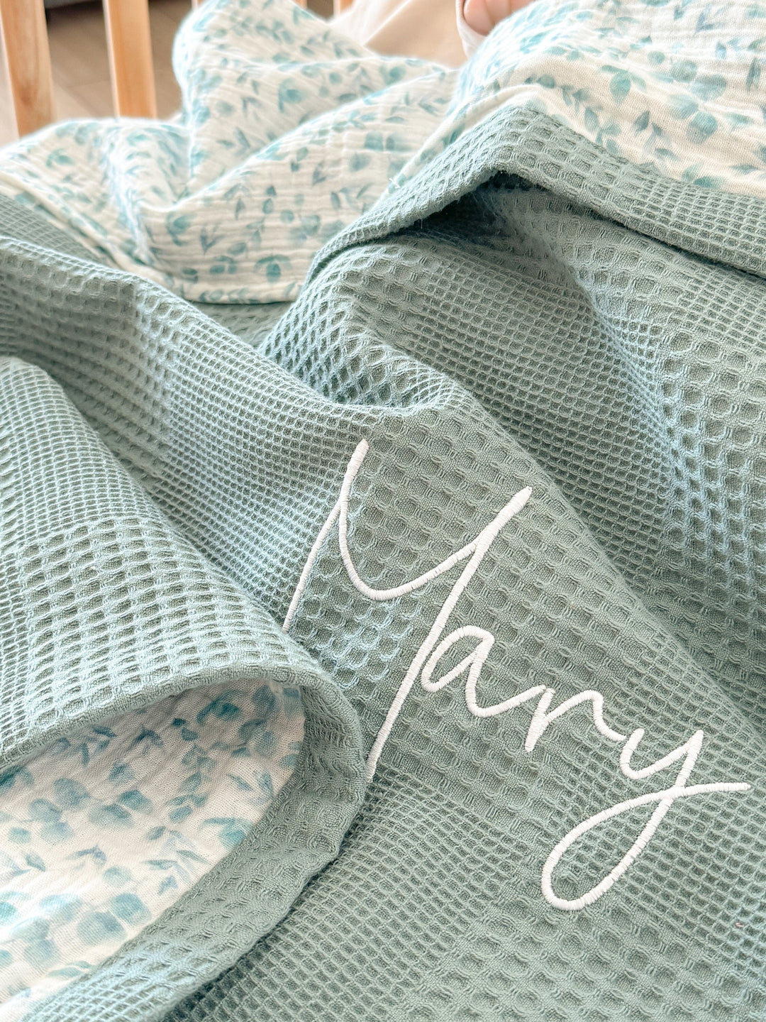 Personalized eucalyptus green baby blanket by Cotton, featuring waffle knit, a reversible leaf print, and the embroidered name "Mary".