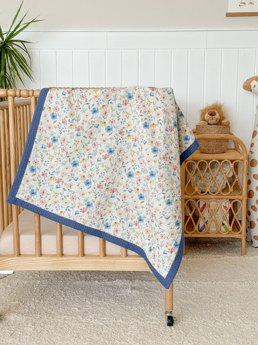 White personalized baby blanket with flower feast pattern by Cotton, featuring a blue waffle-knit border on a crib.