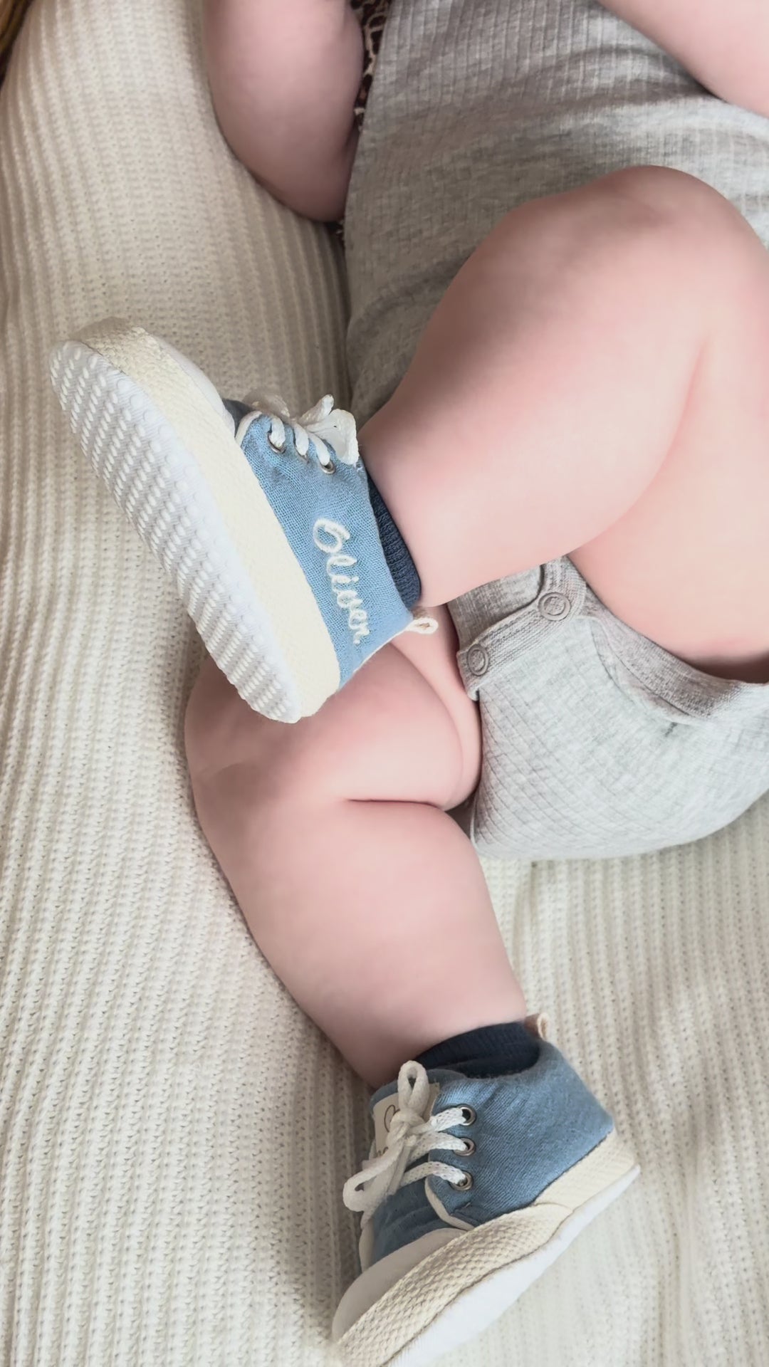 Mouliss personalized denim blue baby shoes with embroidered name, shown on baby in basket