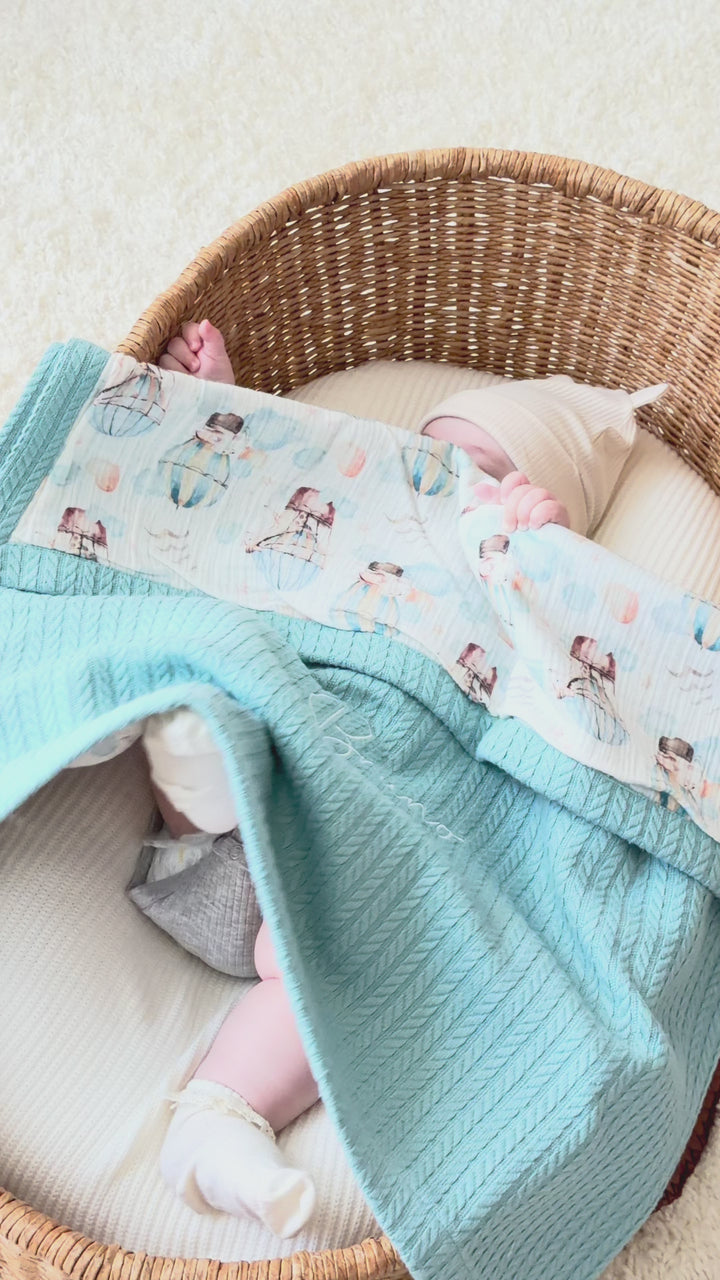 Mouliss personalized blue baby blanket with hot air balloon muslin, embroidered name, shown in basket