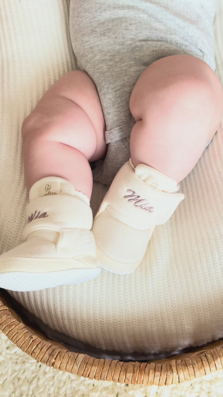 Mouliss personalized cream baby booties with embroidered name, shown on baby in basket